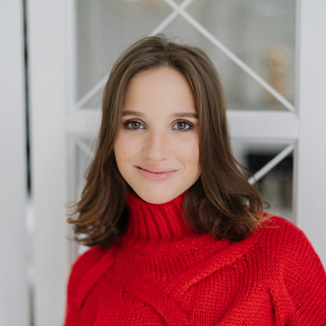 Headshot of charming woman with dark hair, wears knitted sweater, looks directly at camera